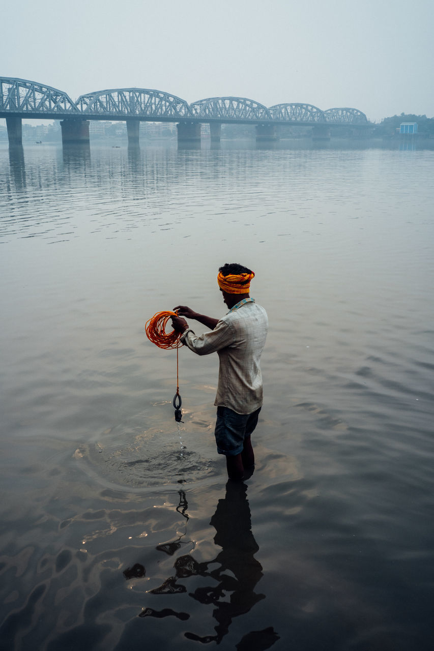 water, one person, real people, sky, standing, lifestyles, nature, men, full length, day, leisure activity, rear view, waterfront, outdoors, holding, occupation, transportation, casual clothing