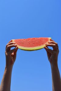 Close-up of hands holding watermelon against blue sky