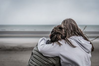 Rear view of sisters with arm around looking at sea