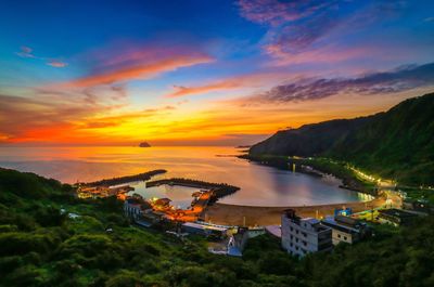 Buildings on mountain by sea against cloudy sky during sunrise