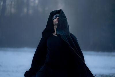 Man wearing mask while standing in snow against trees