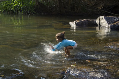 Full length of boy splashing water in river