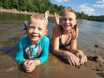Portrait of happy boy and girp siblings laying on the river's shore