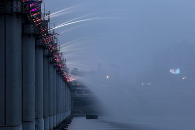 Low angle view of water flowing from bridge in river against sky at dusk