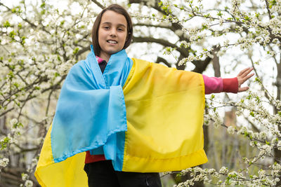 Girl with ukrainian flag standing against tree