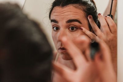 Mirror photo of beautiful young woman putting on makeup