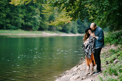 Couple standing by lake against trees