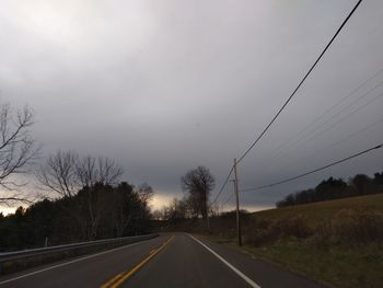 Empty road along trees and landscape against sky