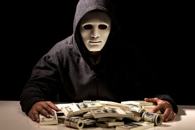 Criminal in mask with currency at table against black background
