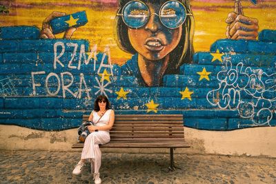 Full length of woman sitting on bench against wall