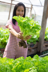 Portrait of smiling woman holding lettuce in greenhouse