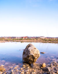 Rocks in calm lake against clear sky