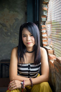 Portrait asian woman lookinging at a camera next to brick wall.