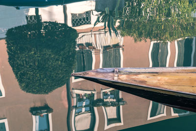 Moored boat on canal, the water reflecting the buildings and trees on shore.