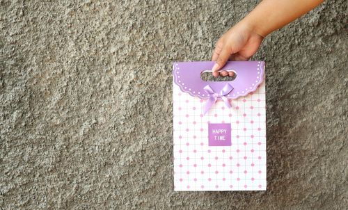 Close-up of hand holding gift bag with text against wall