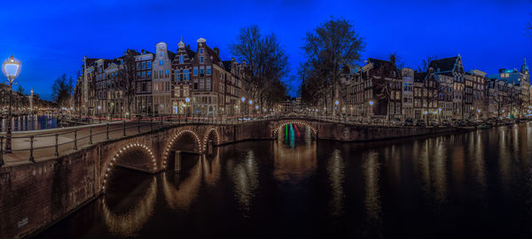 Illuminated bridge over river in city against sky at night