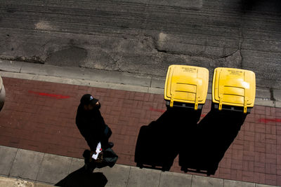 High angle view of man walking by yellow garbage cans on sidewalk