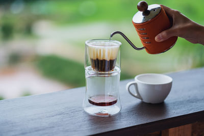 A hand pouring hot water from kettle to make drip coffee with blurred nature background