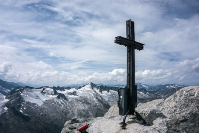 Cross on rock by snowcapped mountains against sky