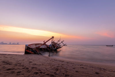 Fishing boat on beach against sky during sunset