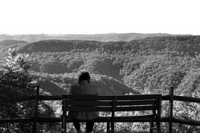 Rear view of woman sitting on railing against mountain