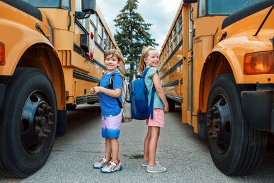 Happy caucasian children boy and girl kids students standing by yellow school bus. education 