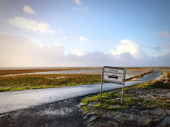 Road sign by sea against sky