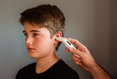 Tween boy getting temperature taken with an ear thermometer.