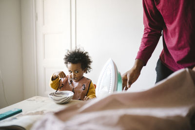 Girl eating from bowl while father ironing clothes