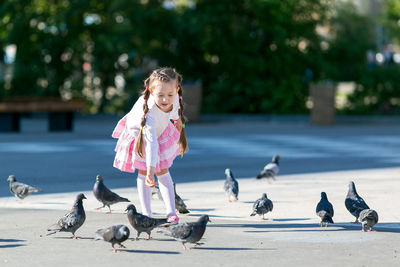 Full length of girl feeding birds while standing on road