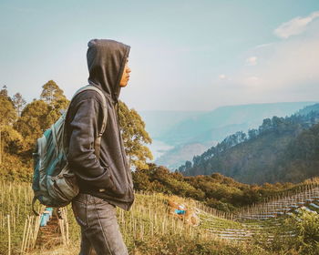 Side view of man standing on land against mountains and sky