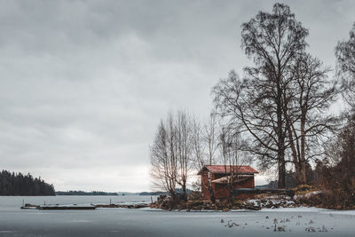 Bare tree and house against sky during winter