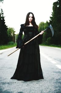 Portrait of young woman standing with scythe on road