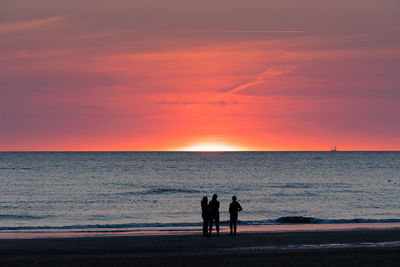 Silhouette people standing on beach against sky during sunset