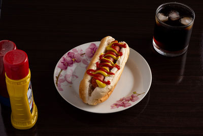 High angle view of hot dog served in plate by drink over black background