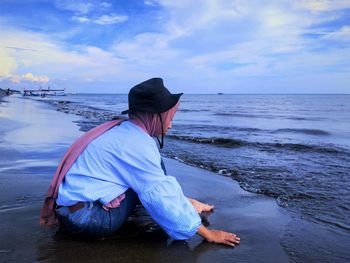 A girl sitting on the beach with a sea and sky view in the background