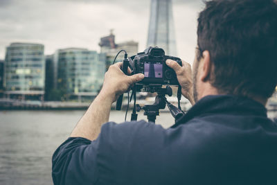 Rear view of man photographing by river in city