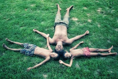 Full length of shirtless young men lying down on field