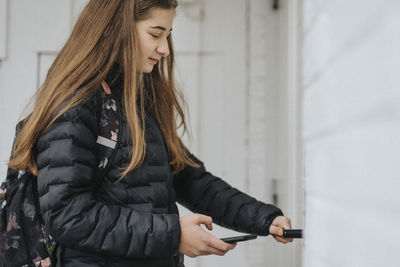 Girl unlocking door lock through smart phone while standing at home
