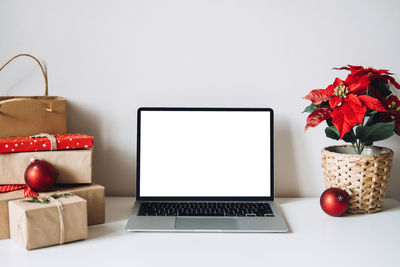 Blank display screen laptop computer with poinsettias christmas flower and gift boxes on white