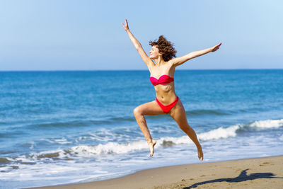 Full length of young woman jumping at beach