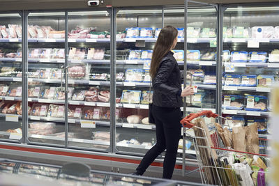 Woman opening glass door of cabinet at refrigerated section in supermarket