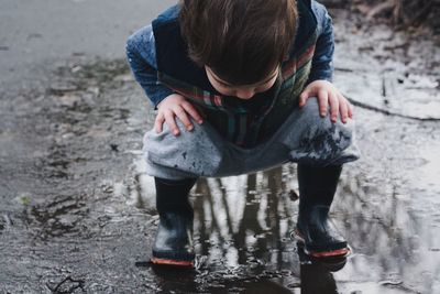 Full length of boy crouching on puddle