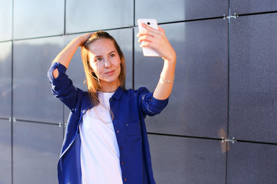 Portrait of young woman standing against wall