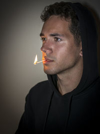 Young man holding burning matchstick in mouth at home