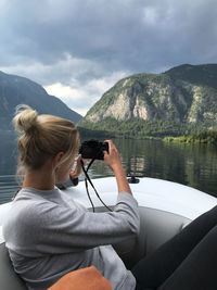 Side view of woman photographing mountain from boat in lake