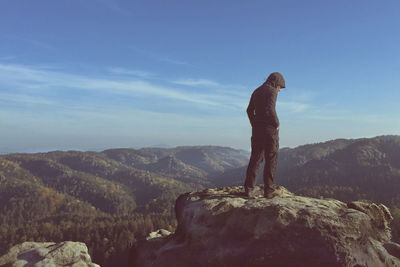 Side view of man standing on rock against sky