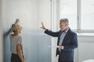 Mature businessman holding documents while discussing with female colleague in new office