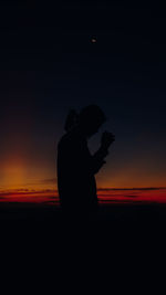 Silhouette woman standing against orange sky during sunset