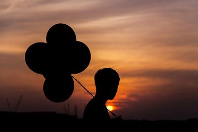 Silhouette man with balloons against sunset